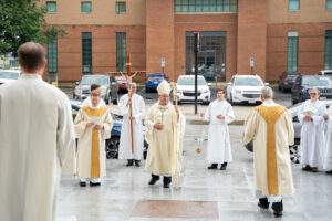 Bishop and servers stand in the rain after Mass, greeting those in attendance