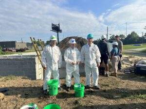 Three volunteers pose in front of the foundation of the home.