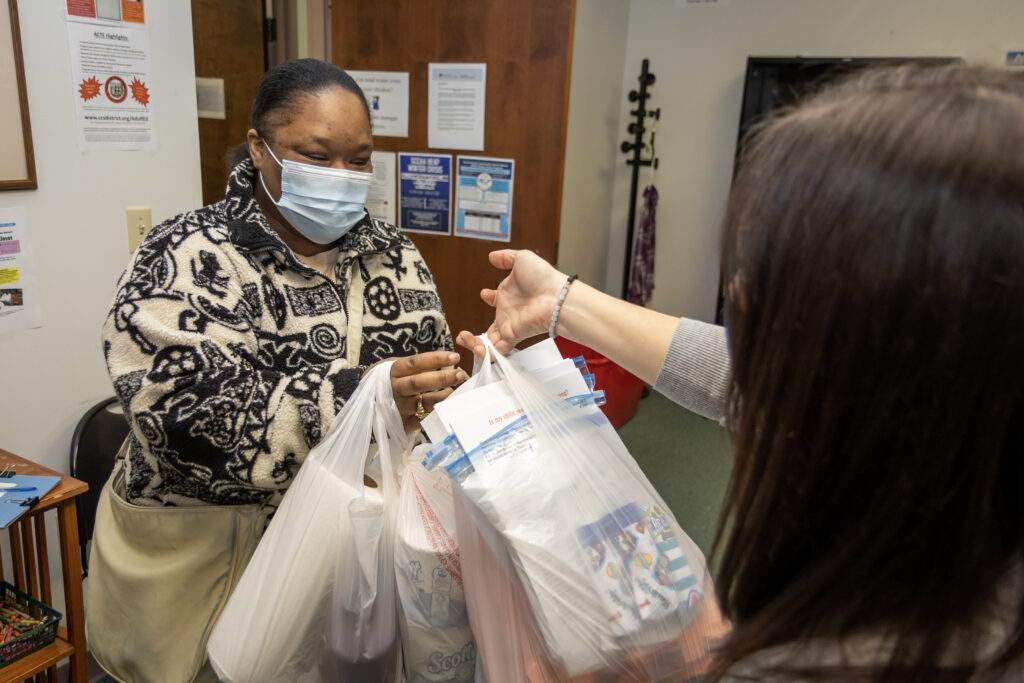 Woman hands shopping bags full of groceries to a mother.