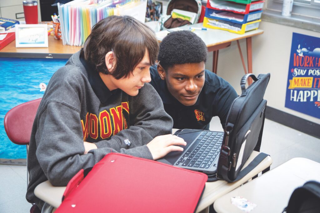 Two students sit, looking at a laptop