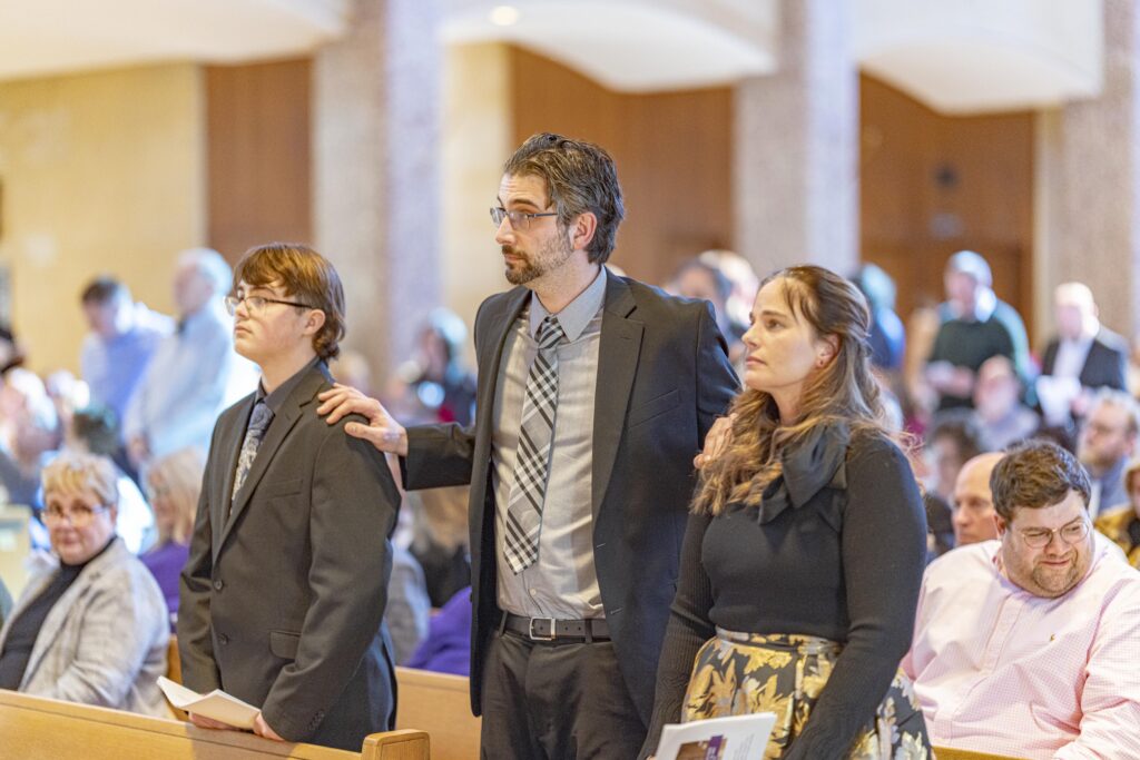 God parent stands with two confirmands at the Rite of Election. Photo by Brian Keith.