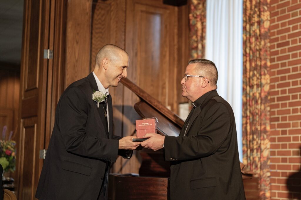 Bishop gives award to man in a black suit at the Golden Apple Awards 2024.
