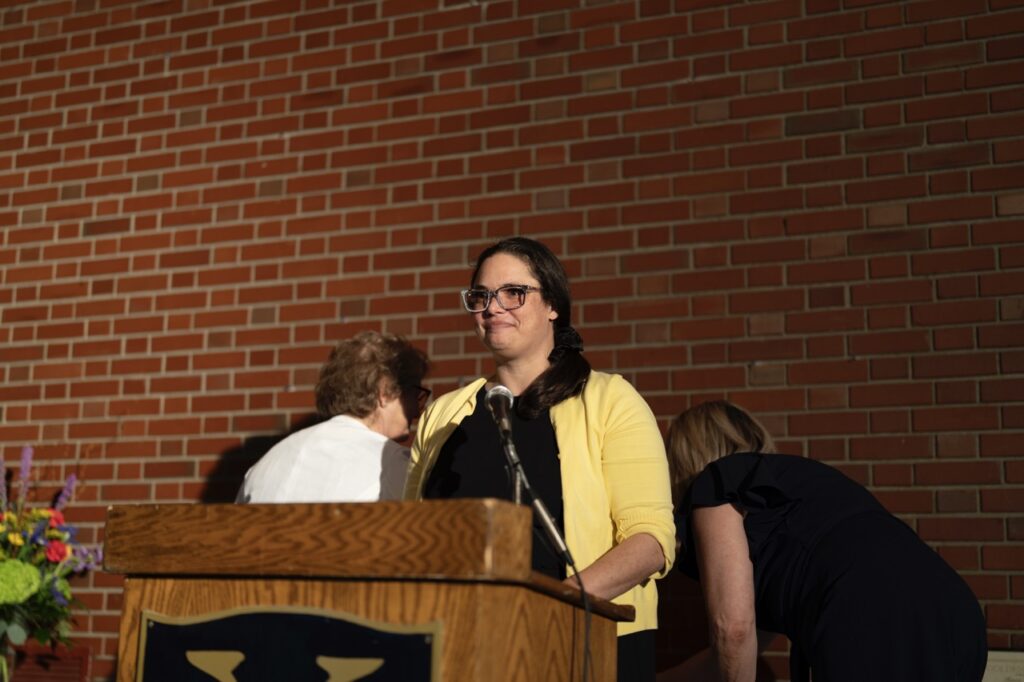 Woman in a yellow sweater speaks at a podium at the Golden Apple Awards 2024.