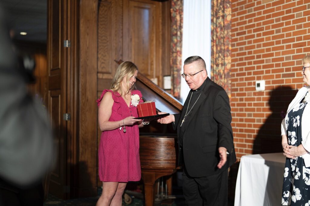 Bishop Bonnar gives golden apple award to woman in a pink dress at the Golden Apple Awards 2024.