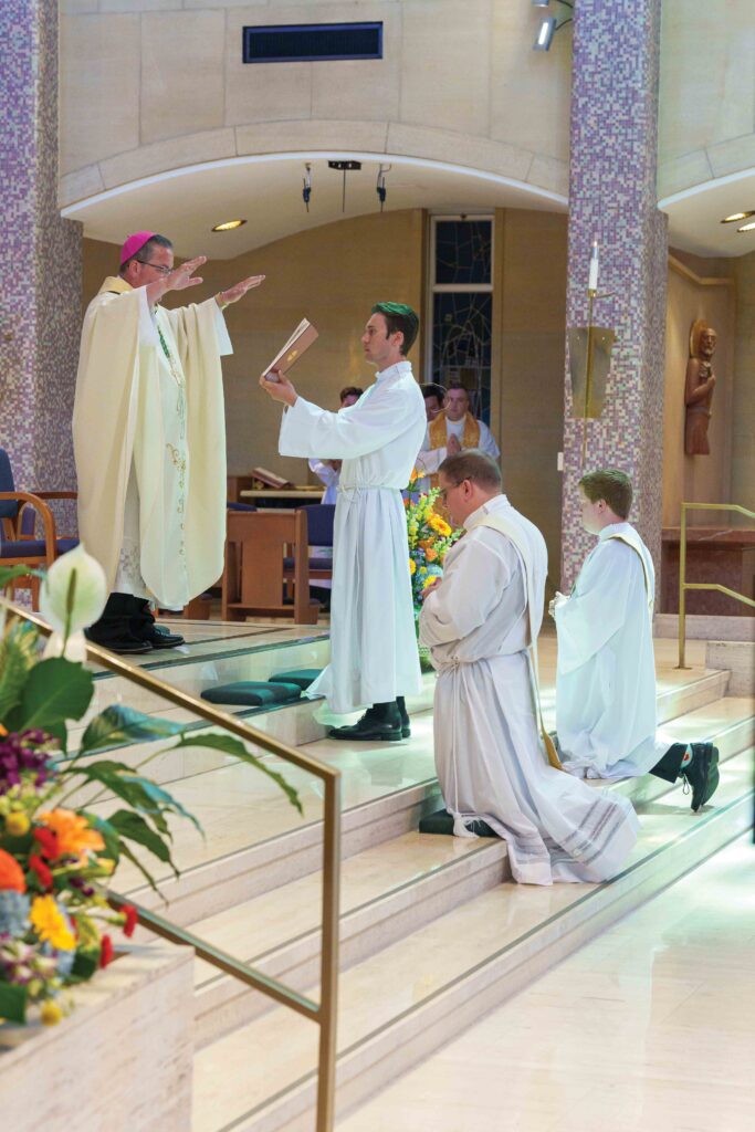 Bishop Bonnar raises his hands in blessing over two new priests