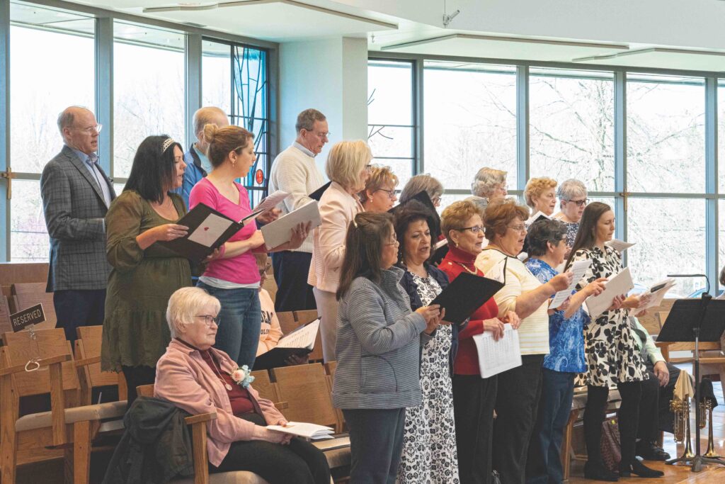 Choir stands on various levels, singing with music raised.