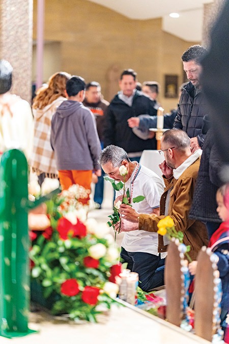 Man places a rose at the foot of an Our Lady of Guadalupe Statue