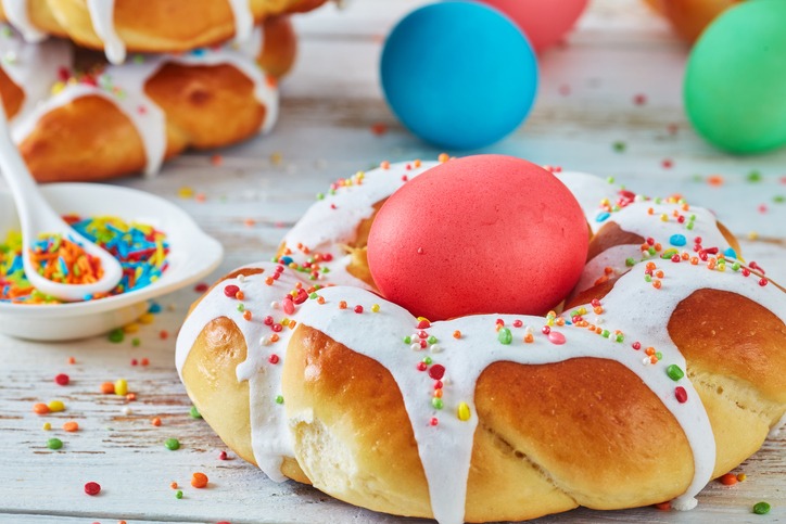 close-up of individual sweet Italian braided Easter Bread Rings glazed around dyed egg and topped with colorful sprinkles on a wire rack, on an old white wooden table, view from above, macro