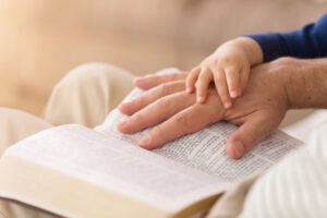 A father and son hold hands over the bible.