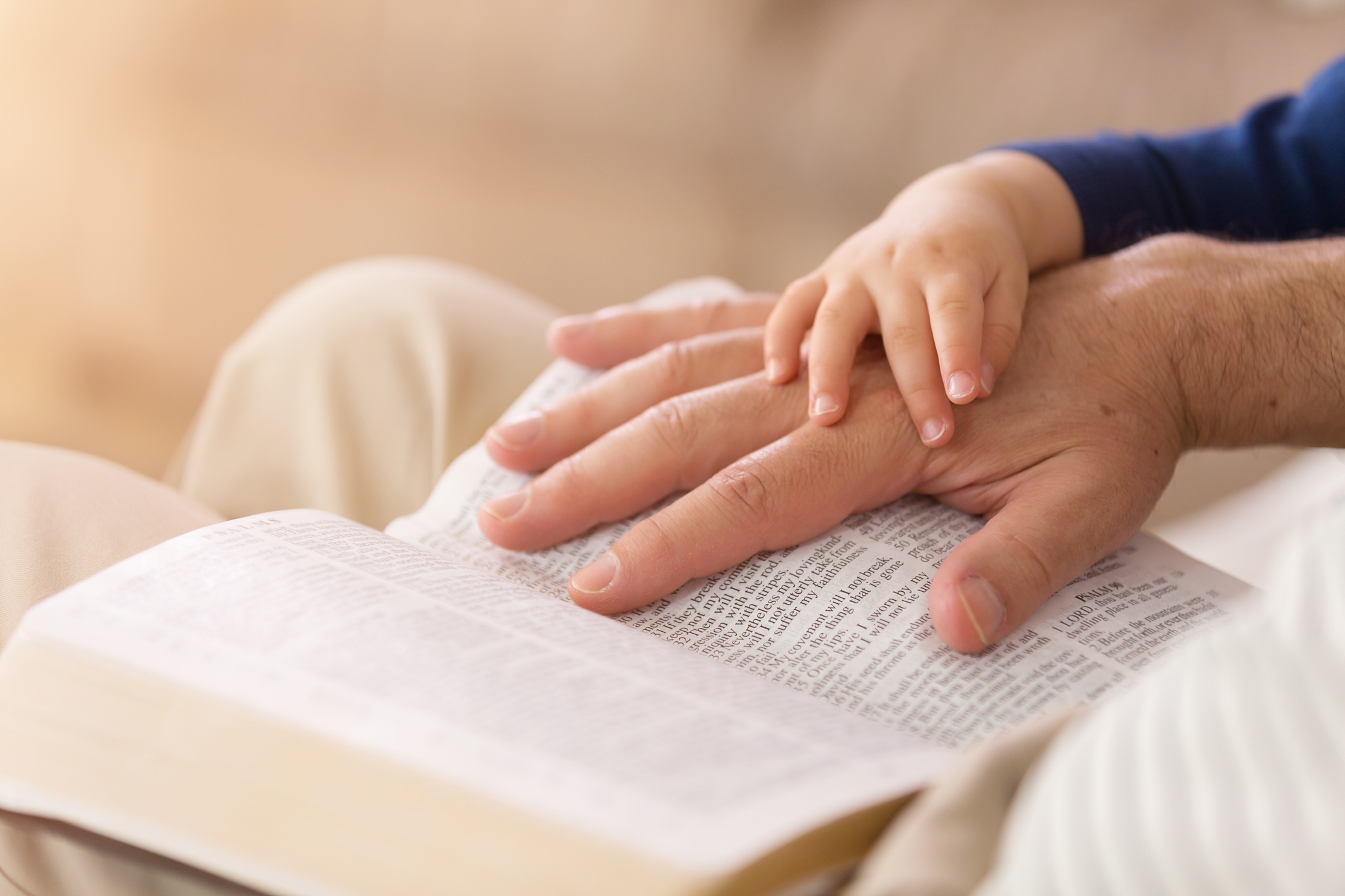 A father and son hold hands over the bible.