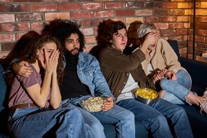A group of friends watching a scary movie at home, raising the question of whether there is a difference between a horror movie and a Christian horror movie.