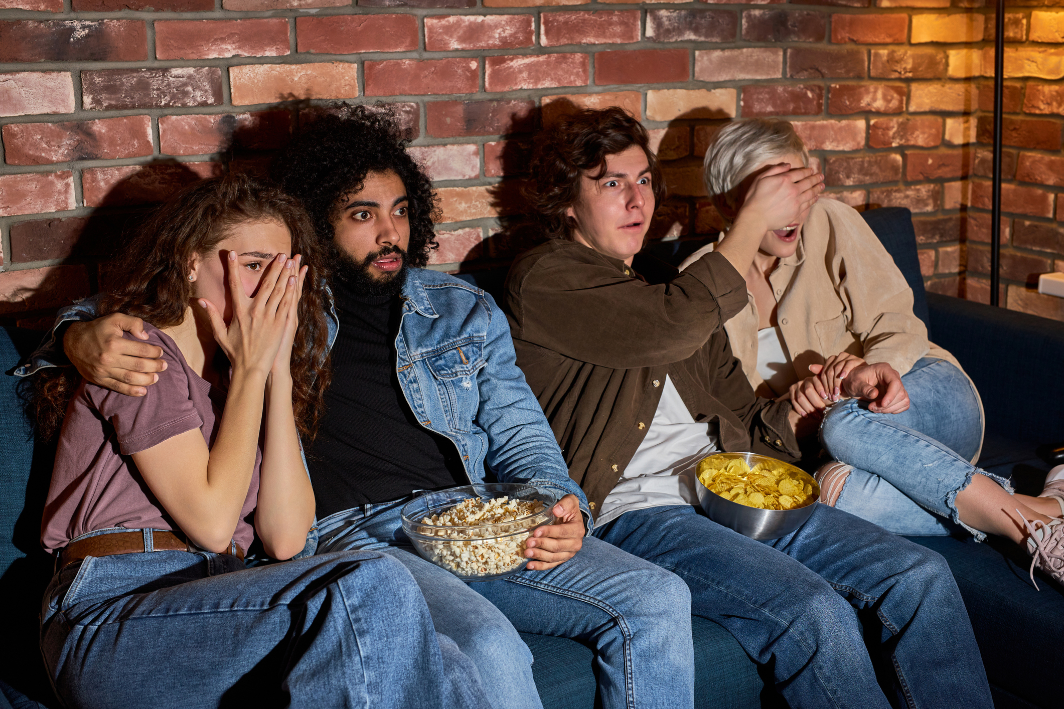A group of friends watching a scary movie at home, raising the question of whether there is a difference between a horror movie and a Christian horror movie.