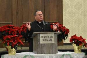 Bishop David J. Bonnar speaks at a podium, surrounded by poinsettias