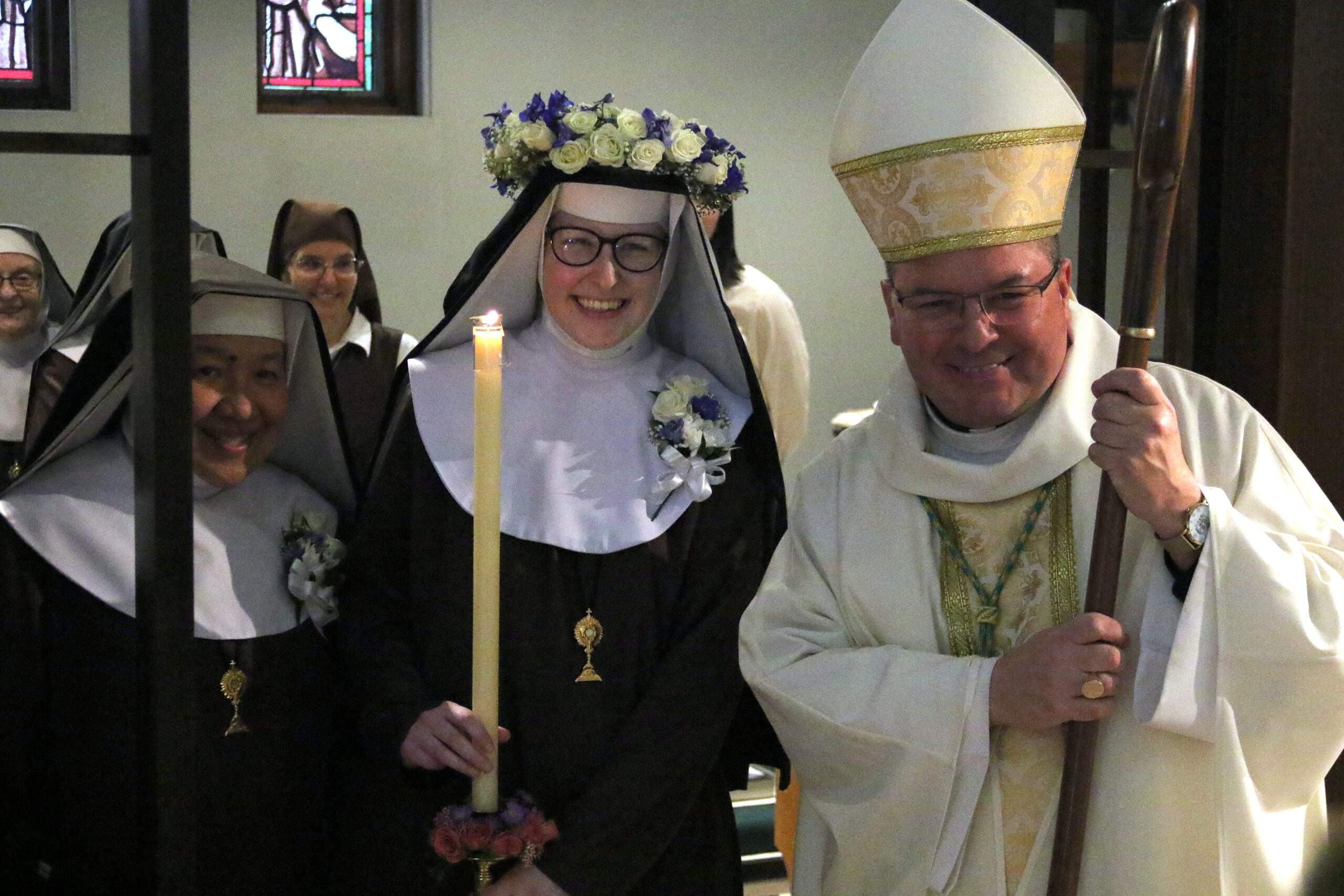 Bishop Bonnar poses for a picture with Sr. Therese Marie, who is wearing a flower crown and holding a candle.