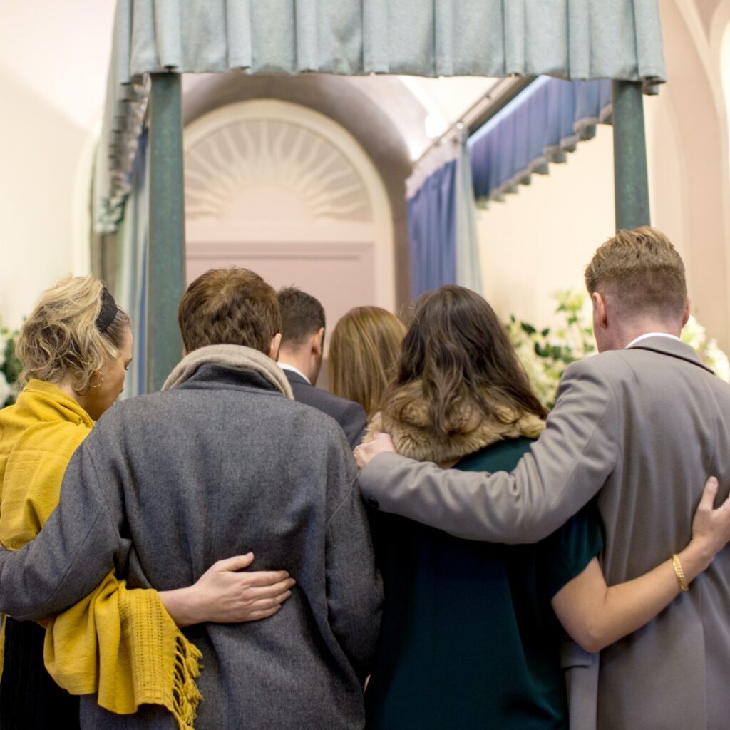 A group of people comfort each other at a funeral ceremony in a crematorium chapel