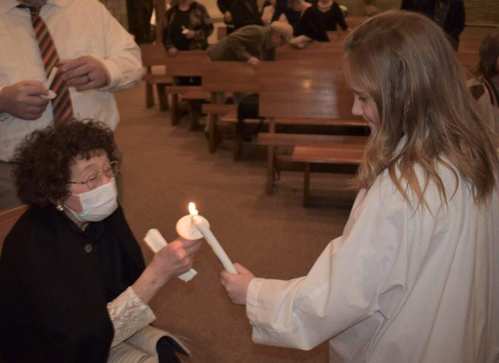 A young confirmand helps an older woman light her candle.