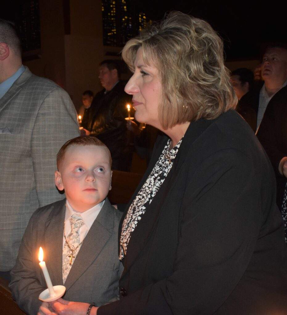 A young boy holding a candle looks up at an older woman.