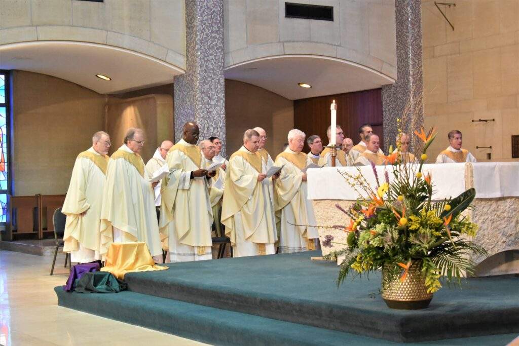 A large group of priests stands to the left of the altar during the Chrism Mass.
