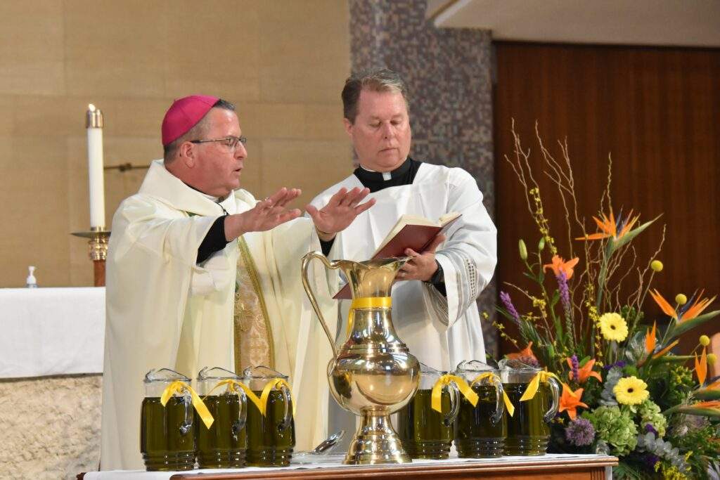 Bishop Bonnar stands with his hands over several vessels of oil, blessing them.