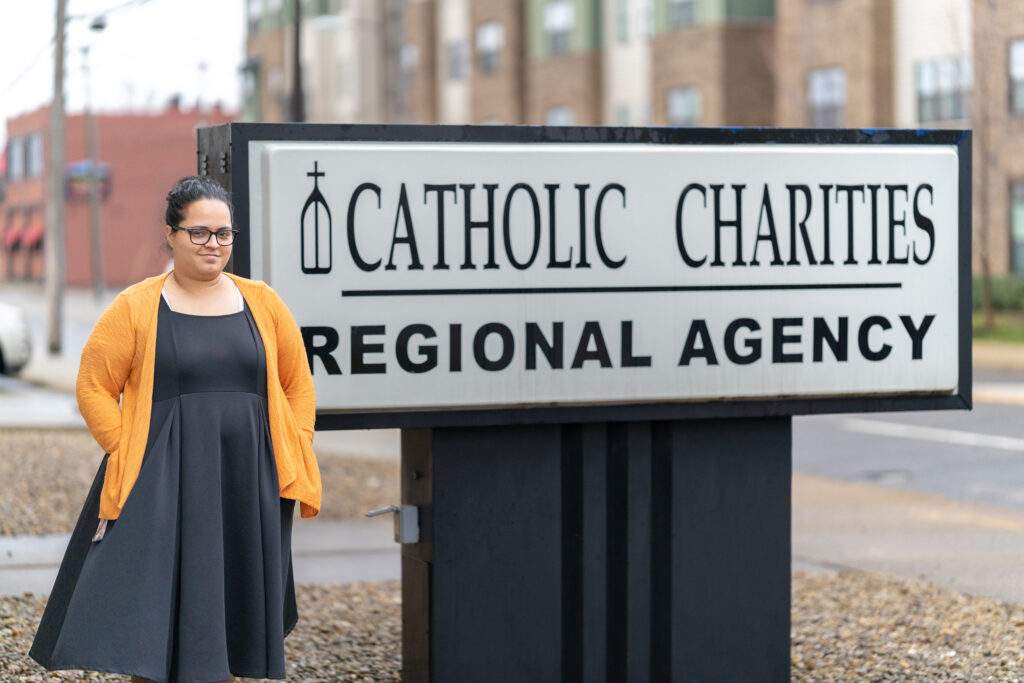 Wanda poses in front of the Catholic Charities Regional Agency sign.