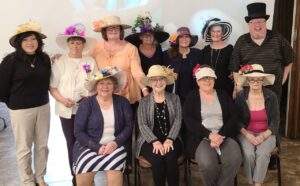 Ten women and Fr. Misbrenner pose with hats on at the Kentucky Derby party.