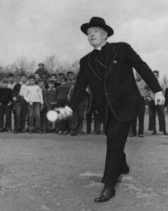 Bishop McFadden, wearing a black bowler hat, throws the first pitch at a baseball game.