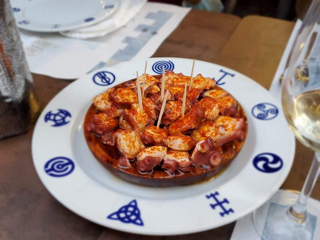 Spicy red seafood dish, placed on a white charger plate with decorative blue symbols around the edges.