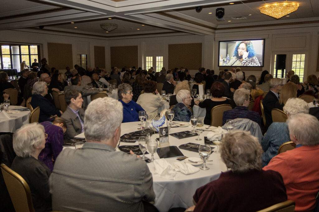 A sold-out crowd sits at their tables, watching a video about Catholic Charities' good works.