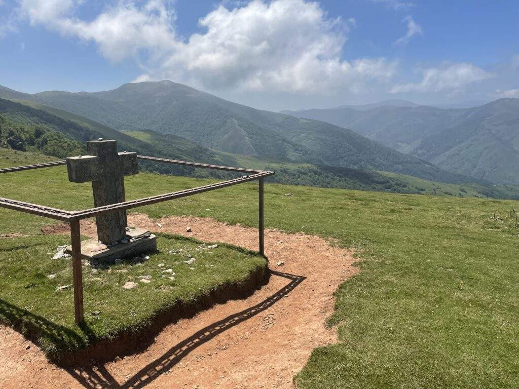 A statue of a cross with the Pyrenees Mountains in the background.
