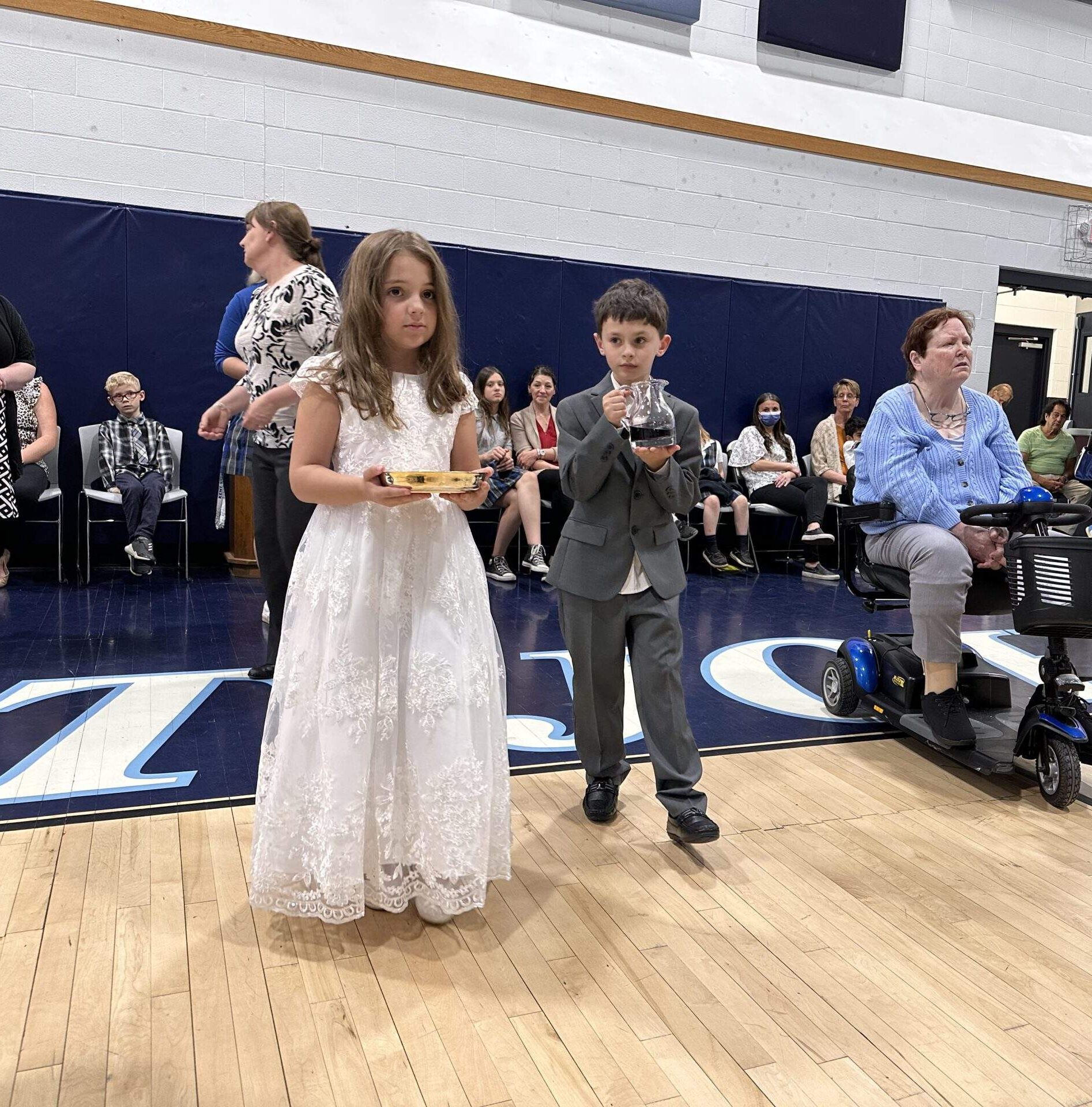 Young boy and girl in first holy communion attire bring forward the gifts during the offertory.