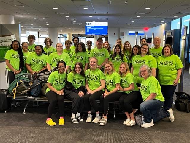 Group poses in the airport, in matching green SOS shirts