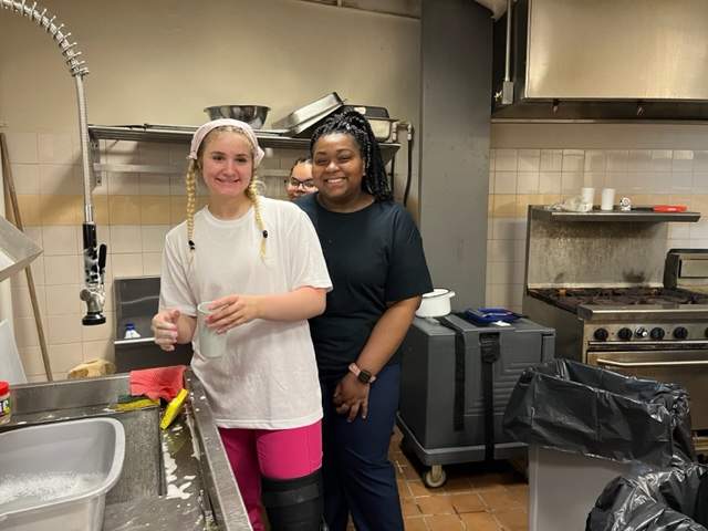 Three female students pose in a kitchen, where they are washing dishes.