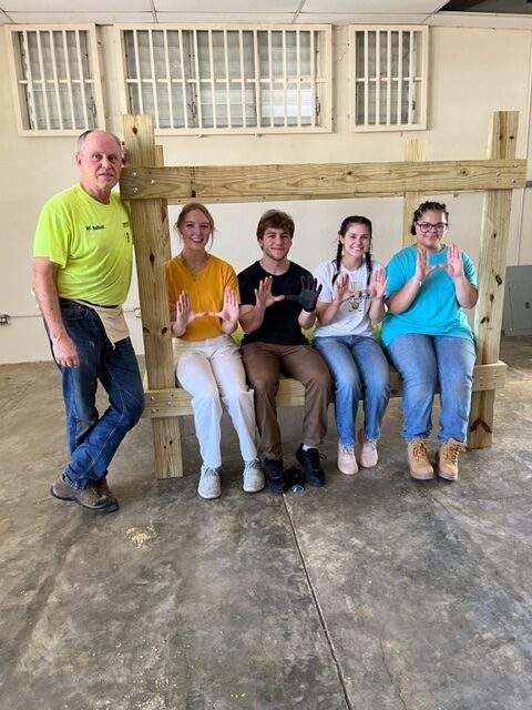 four students and one chaperone pose within a wooden frame they built