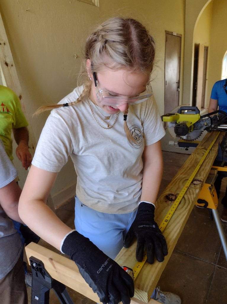 Young female student measures plywood for a construction project.