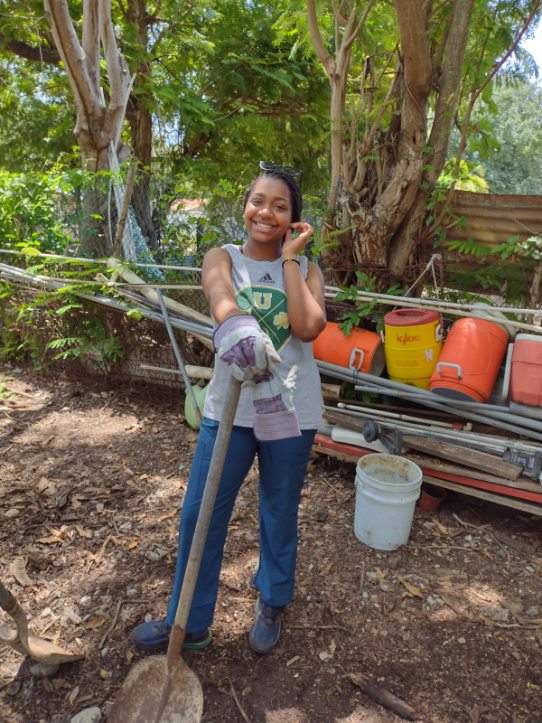 Young female student smiles, with shovel in hand.