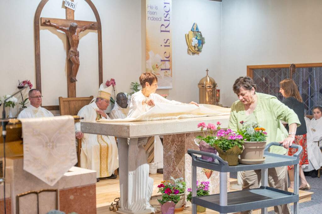 Lay people decorate the altar with a cloth and flowers during altar blessing at Sacred Heart Parish in Rock Creek. Photo by Brian Keith.