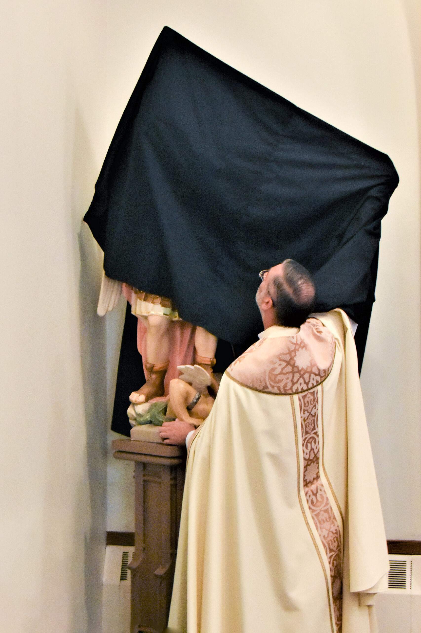 Father Conoby unveils the St. Michael Statue from St. Michael Church in Windham (closed in 2022) at its new home at St. Ambrose Parish in Garrettsville.