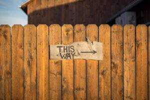 sign on a wooden fence reading "this way" with an arrow