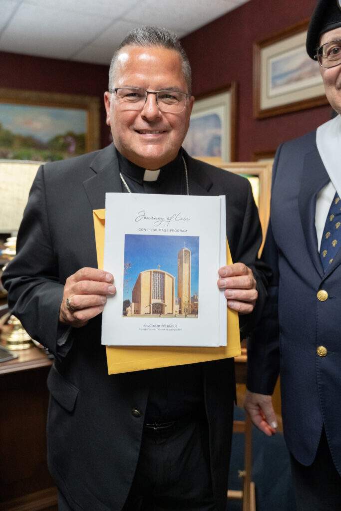Bishop poses with program book for pilgrimage