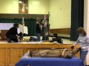 Three women clean different statues in the parish's community center.