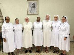 seven Oblate sisters in white habits stand beneath a painting of Mother Maria Theresa Cassini