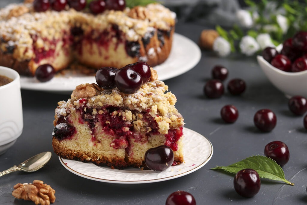 Homemade cherry pie with shtreisel and walnuts on white plate on a dark concrete background, piece of cake is located in the foreground