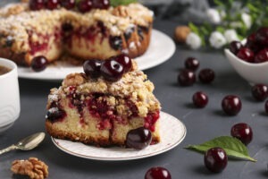 Homemade cherry pie with shtreisel and walnuts on white plate on a dark concrete background, piece of cake is located in the foreground