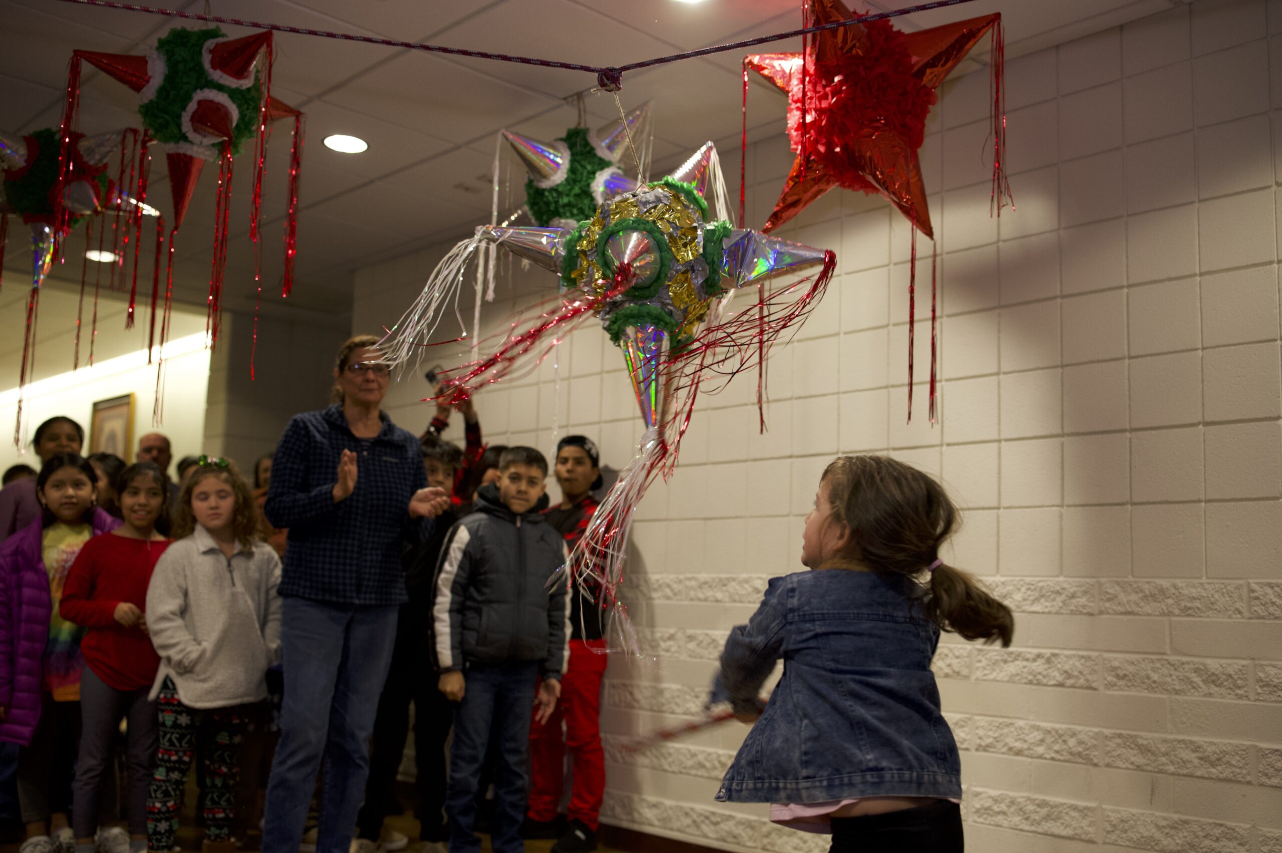 Young girl hits a piñata in front of a crowd at Las Posadas celebration