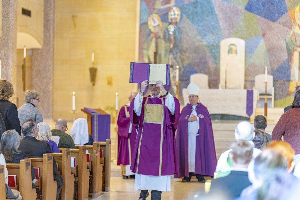 Deacon raises book for all to see at the Rite of Election. Photo by Brian Keith.