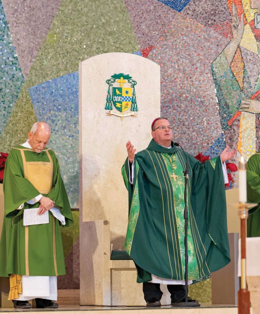 Bishop bonnar stands with arms raised in front of the cathedra. Photo by Brian Keith