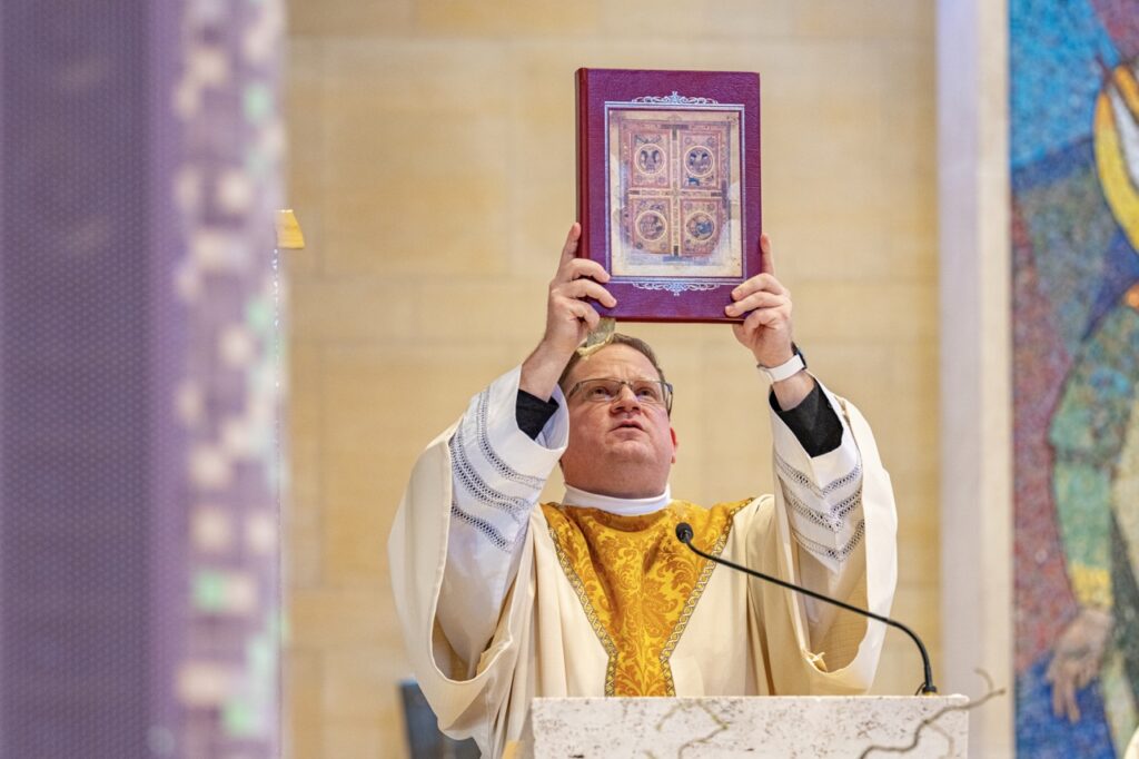 Deacon Kevin raises the bible at the ambo during Holy Thursday 2024. Photo by Brian Keith.