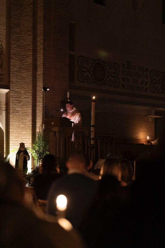 Priest reads the Gospel by candle light at the Easter Vigil 2024 at St. Dominic's. Photo by Brian Keith.