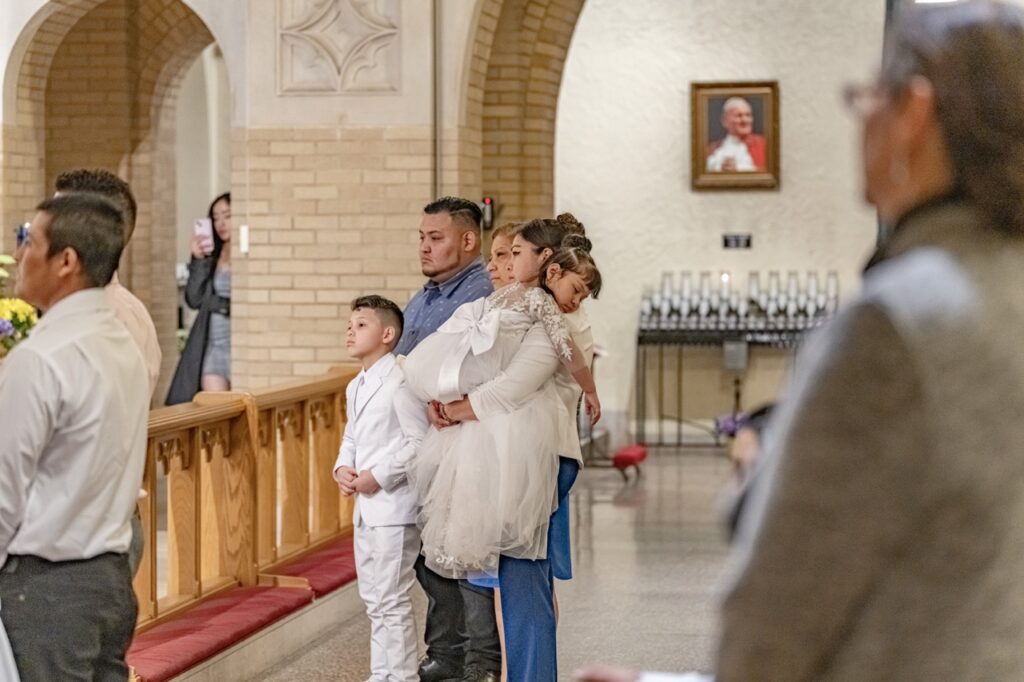 First Holy communion candidate sleeps, over mother's shoulder at the Easter Vigil 2024 at St. Dominic's. Photo by Brian Keith.