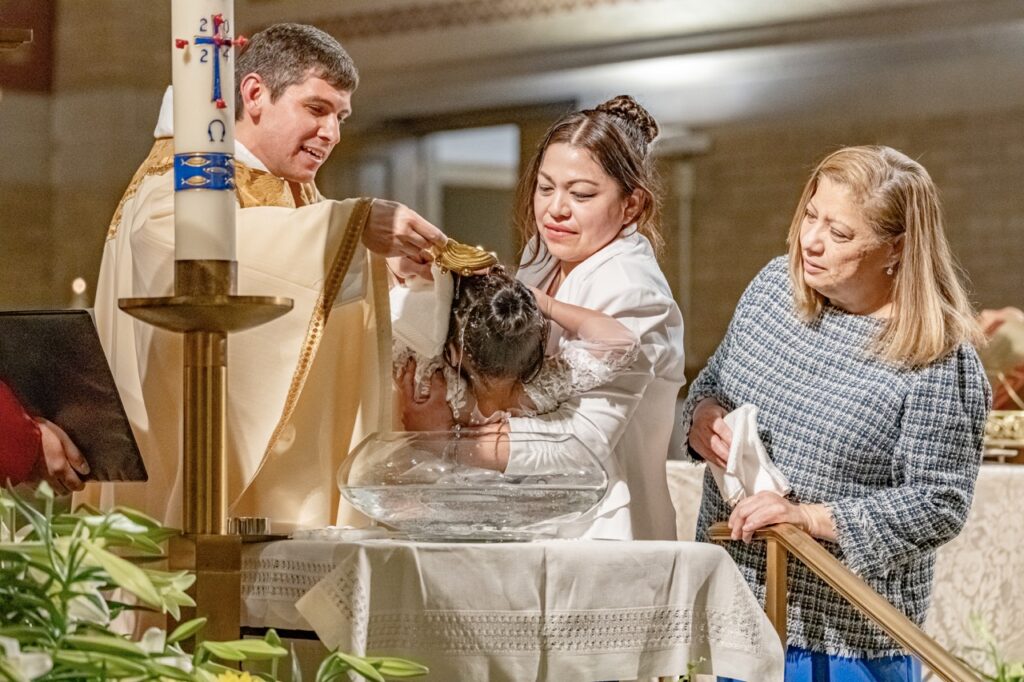 Mother holds child over baptismal font at the Easter Vigil 2024 at St. Dominic's. Photo by Brian Keith.